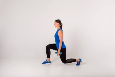 Sporcu kadın, beyaz arka planda dambıllarla çömelme egzersizleri yapıyor. Yan görünüm.