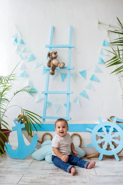 Beyaz tişörtlü ve kot pantolonlu neşeli bir çocuk ahşap bir teknenin arka planında kameraya bakıyor.