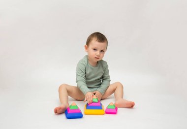 Yeşil elbiseli küçük bir çocuk beyaz arka planda renkli bir piramitle oynuyor ve yazı için yeri var. Erken çocuk gelişimi