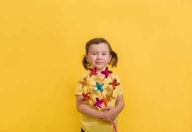 Küçük gülümseyen bir kızın portresi, sarı izole bir arka planda oyuncak esinti tutuyor, mesaj için yeri var..