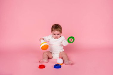 Küçük kız pembe arka planda piramit oyuncakları toplamayı öğreniyor.