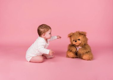 Pembe izole edilmiş arka planda pelüş bir köpek oyuncağıyla oynayan küçük bir kız.