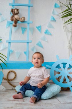 Küçük bir çocuk yerde, tahta bir teknenin yanında oturuyor.