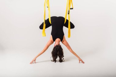 Beyaz bir arka planda hamakta ters dönmüş anti-yerçekimi yoga pozu veren bir kadının arka görüntüsü.