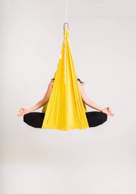 Bir kadın sarı bir hamakta oturuyor Padmasana pozunda beyaz bir arka planda