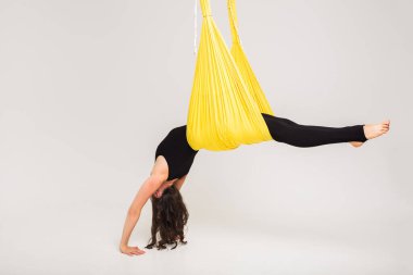 Bir kadın beyaz arka planda hamak kullanarak amuda kalkar.