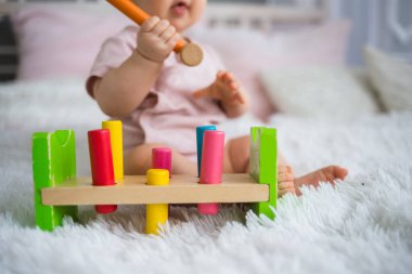 Yatağın üzerinde tahta bir oyuncakla oynayan küçük bir kızın fotoğrafını çek.