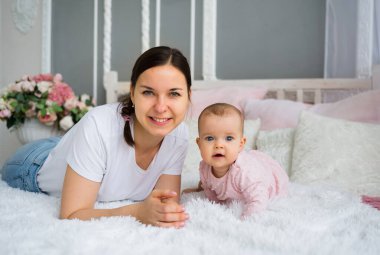 Anne esmer ve küçük kızı yatağa uzanıp kameraya bakıyor.