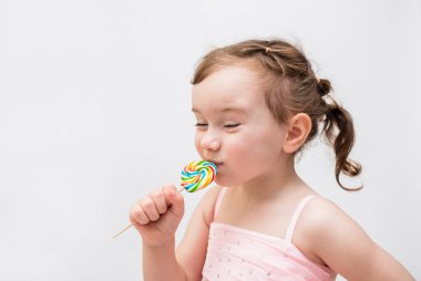 Çubukta lolipopu olan beyaz arka planda bir kız. Renkli şekerli pembe elbiseli at kuyruklu bir kız..