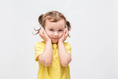 Beyaz arka planda sarı tişörtlü bir kız. Küçük kız kulaklıkla müzik dinliyor..