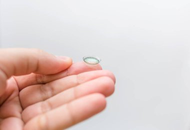 Parmağında mercek var. Elindeki renkli mercek. Beyaz arka planda renkli lensler. Miyop. Boş bir arkaplan ile beyaz arkaplan