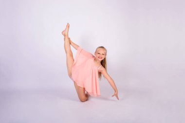 Şeftali rengi mayo giymiş sarışın bir jimnastikçi kız jimnastik pozu verir ve beyaz izole bir arkaplanda mesaj için yer olan kameraya bakar.