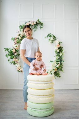 Anne beyaz arka planda çiçekli küçük kızını tutuyor.