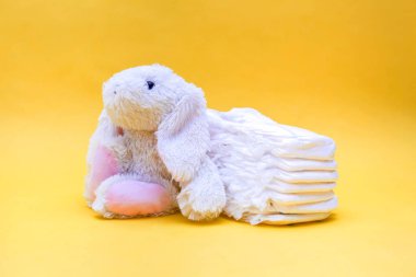 Beyaz bebek bezi ve sarı arka planda bir tavşan. Sarı arka planda tavşan oyuncağı. Arka planda arka planda bebek bezi ve boş bir alan..