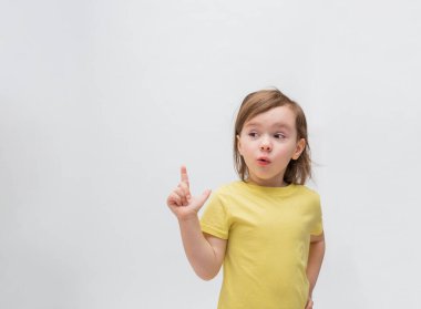 Beyaz arka planda küçük bir kız. Sarı tişörtlü, gevşek saçlı tatlı kız. Küçük kız şaşırdı. Boş alan