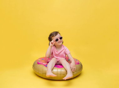 Gözlüklü küçük bir kız daire çiziyor. Donut şeklinde bir balon. Sarı arka planda güneşlenen tatlı bir kız..