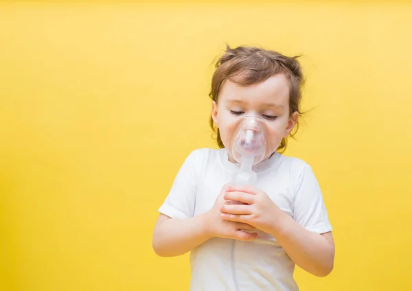 Cute little girl in a white t-shirt on a yellow background. A little girl is breathing through a mask. Diseases of the upper respiratory tract. Inhalations.