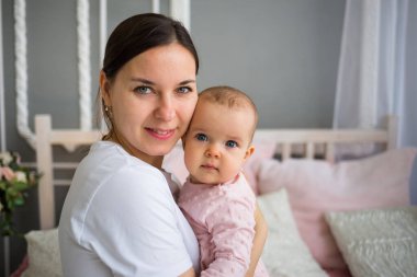 Esmer bir annenin portresi. Küçük kızını odada yatakta kucaklıyor.