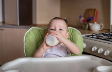 Bebek bir beslenme sandalyesinde oturur ve bir şişeden içer.