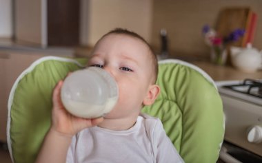 Bebek bir beslenme sandalyesinde oturur ve bir şişeden içer.