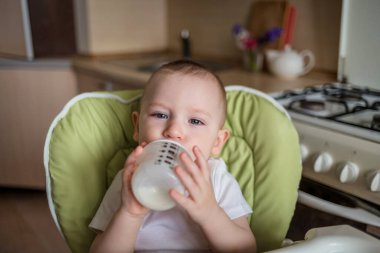 Bebek bir beslenme sandalyesinde oturur ve biberondan içer. Bebek doğru beslenmeyi yiyor. Ekolojik ürünler