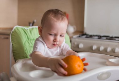 Bebek sandalyede oturur ve portakal yer.