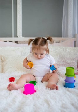 Beyaz elbiseli akıllı kız yatakta oturur ve bir piramit toplar.