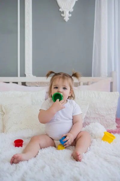little girl in a white bodysuit plays on the bed with colorful toys