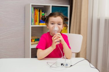 Küçük kız oturur ve odada bir nebulizatörle nefes alır.