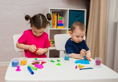 Küçük bir kız ve bir oğlan odada bir masada plastikle oynuyorlar.