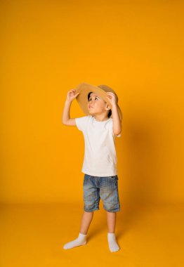 Hasır şapkalı küçük bir çocuk sarı arka planda duruyor ve mesaj için yeri var.