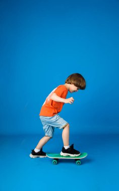 Tişörtlü ve şortlu küçük bir çocuk mavi arka planda kaykaya biniyor ve mesaj için yeri var.