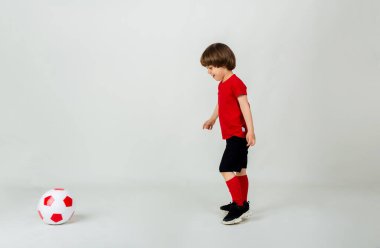 Küçük futbolcu beyaz arka planda bir futbol topuyla oynar.