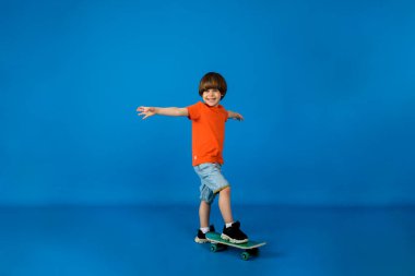 Mutlu küçük çocuk mavi bir arka planda kaykayla duruyor ve mesaj için yer var.