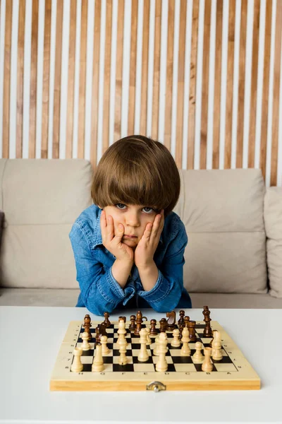 Menino fofo de 5 anos jogando xadrez sozinho em seu quarto em casa