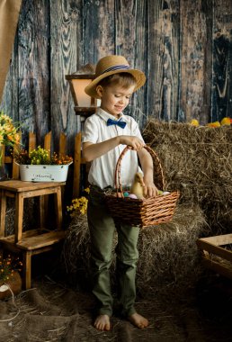 Paskalya süslemelerinde renkli yumurta sepeti olan gömlek, papyon ve hasır şapkalı küçük bir çocuk.