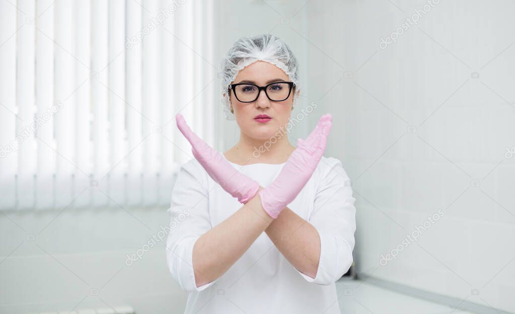 a female doctor in a white medical suit, a cap stands in the office and shows a forbidding gesture with her hands