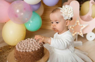 Kirli suratlı ve elleriyle pasta yiyen küçük bir kızın portresi. Birinci doğum günü
