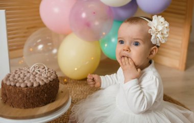 Şok olmuş küçük kız, arka planda kremalı pasta yiyor. Pasta kazası geleneği.