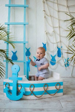 Çizgili tulumlu bebek tahta bir kayıkta oturur ve direksiyonu deniz dibinde tutar. Yaz seyahati