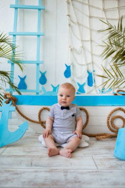 Küçük bir denizci, ahşap bir teknenin yanında, deniz arka planında, mesaj atabileceği bir yerde oturuyor. Yaz seyahati