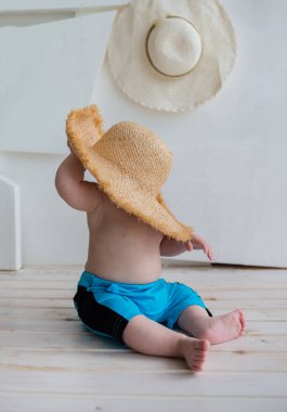 Mavi şortlu bebek beyaz arka planda hasır şapka takıyor ve mesaj için yer açıyor. Yaz arkaplanı