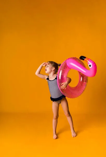 Çizgili mayo giymiş neşeli küçük sarışın kız pembe şişirilebilir bir daire tutuyor ve mesajlaşmak için yeri olan sarı bir arka plana bakıyor. Yaz arkaplanı