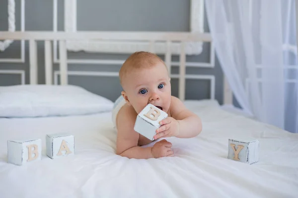 Beyaz küplü beyaz bir yatakta, beyaz bir battaniyenin üzerinde, mavi gözlü, beyaz bir oğlan çocuğu yatıyor. Diş çıkarma.