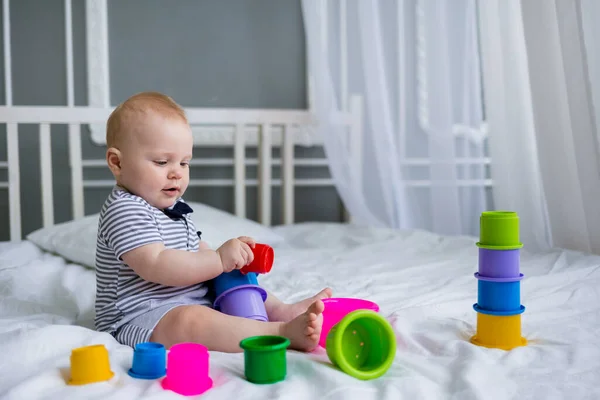 Bebek beyaz bir yatakta plastik bir piramitle oynuyor. Erken çocuk gelişimi