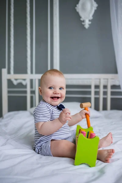 Szczęśliwy Chłopiec Bawi Się Drewnianą Zabawką Białym Łóżku Patrzy Kamerę — Zdjęcie stockowe