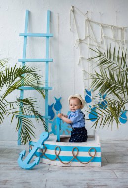 Hasır şapkalı küçük bir denizci arka planda, ahşap bir teknede oturuyor.