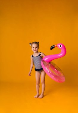 Çizgili mayo giymiş komik sarışın ayakta duruyor ve elinde sarı arka planda flamingolu pembe şişirilebilir bir daire tutuyor.