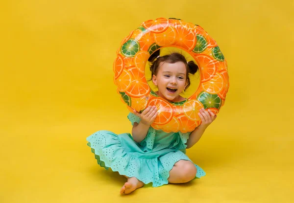 eğlenceli küçük kız sarı arka planda şişirilebilir bir yüzme çemberiyle oynuyor.