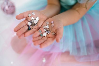 Bir çocuğun ellerinde neşeli bir arka planda gümüş konfeti yıldızları var.